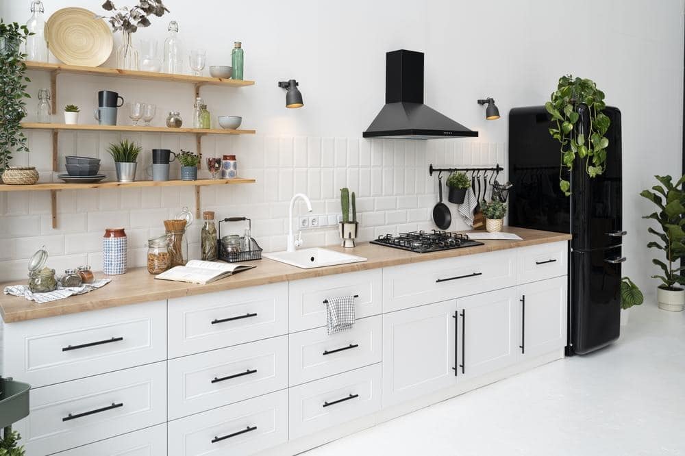 white kitchen with black fridge, wooden counter and white cabinets, drawers