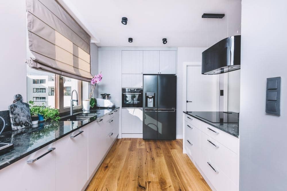 white kitchen with galley shaped layout that has wooden flooring