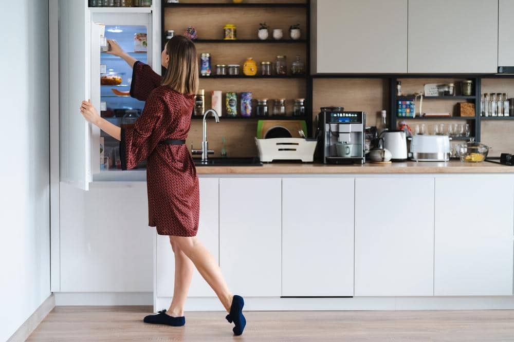 a woman looking for something in fridge in a kitchen