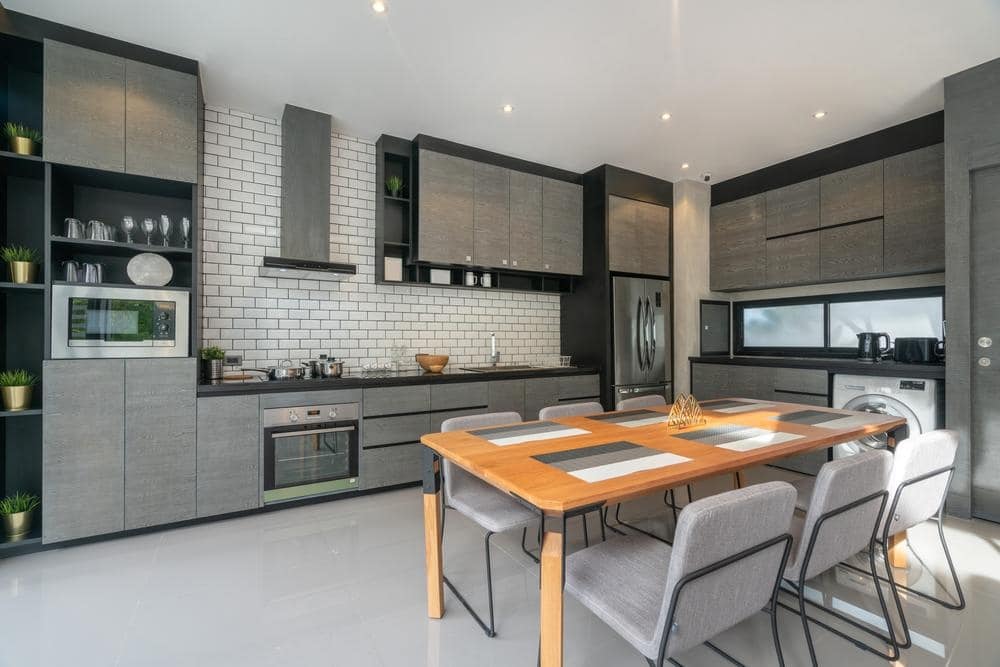 large airy kitchen with grey cabinets and wooden table with chairs next to it