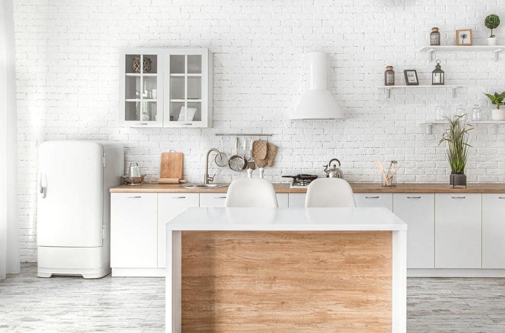 white kitchen with wooden and white island and cabinets next to small white fridge